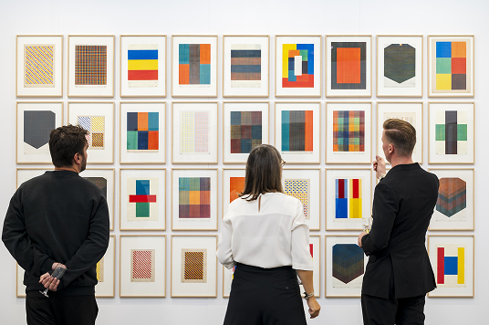 Visitors viewing a wall of artworks at Art on Paper
